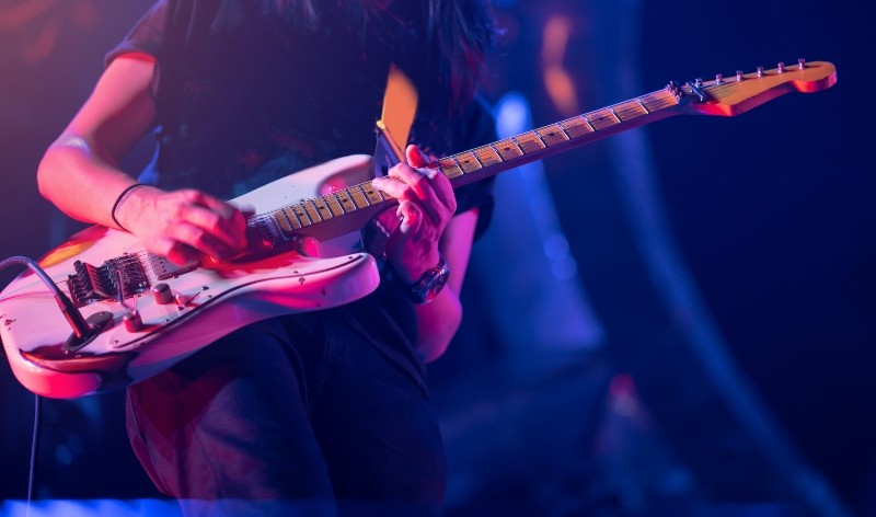 Guitarist playing his vintage guitar on stage. Guitar solo under blue, orange, purple lighting. Selective focus.