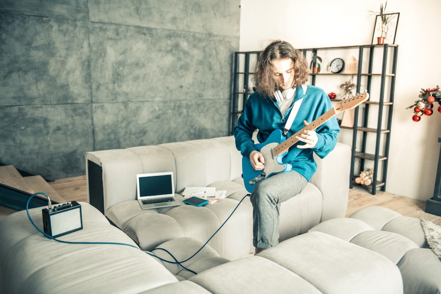 Ein Gitarrist übt im heimischen Wohnzimmer mit einem Übungsamp im Lunchbox-Format Übungsamp für die Gitarre