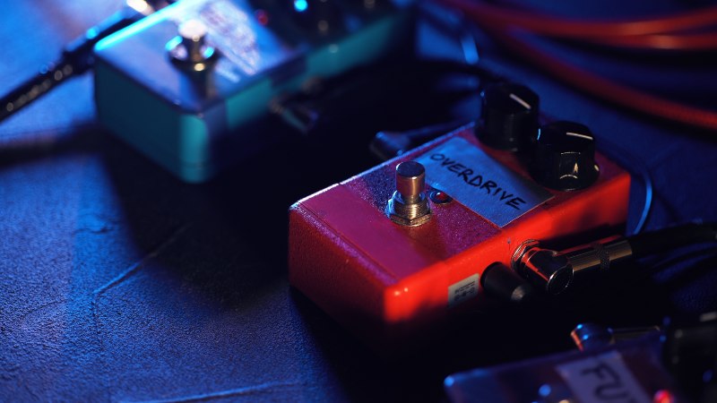 On the floor, the pedals of several effect devices are placed; on one of them is the overdrive for adjusting the guitar sound
