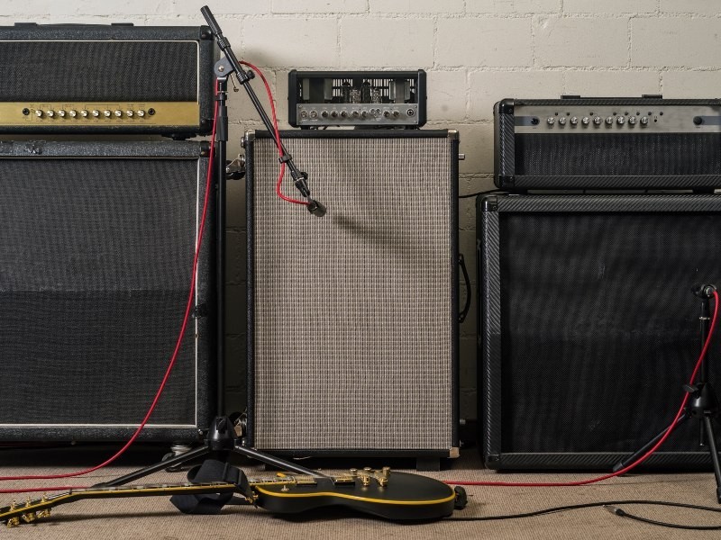 In a rehearsal room, several amplifiers are positioned along a wall, with a microphone placed in front to capture the sound
