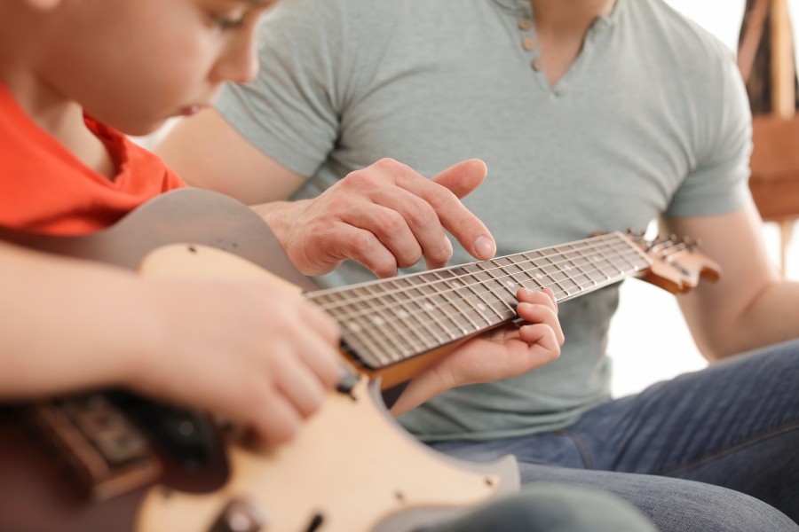 Boy learns electric guitar with teacher/father