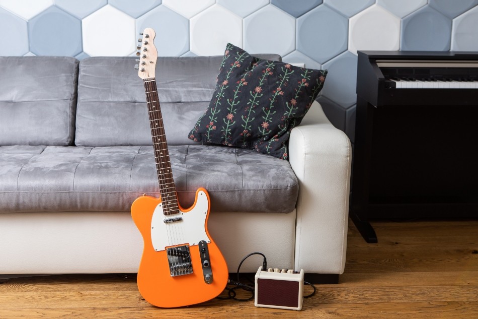 E-Gitarre lehne an Sofa, kleiner Amp steht daneben - kleiner Digital-Verstärker