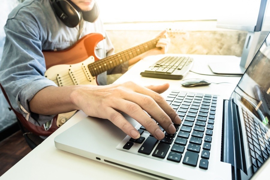 Junger Mann mit E-Gitarre am Laptop - Hybridverstärker und Modeling-Amps