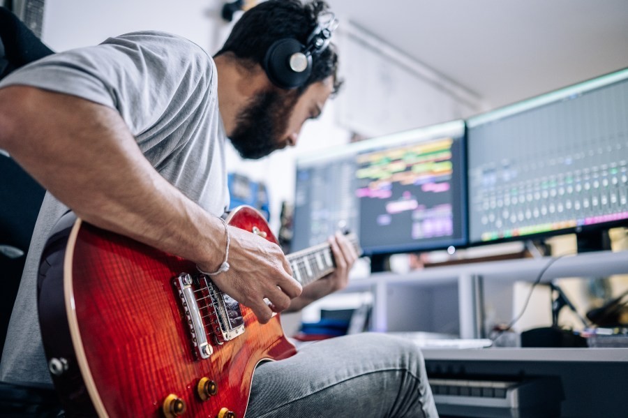 Junger Mann mit E-Gitarre in einem Musik-Studio - Loadbox oder Booster für Amps